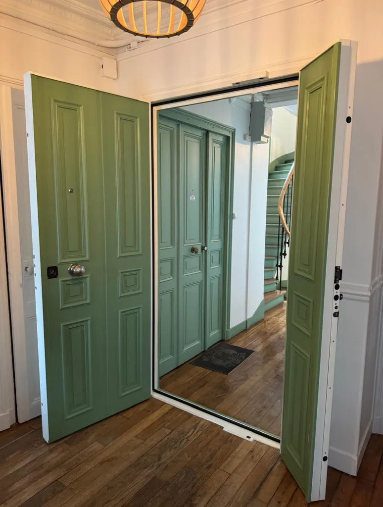 Porte blindée deux vantaux laquée verte, ouverte sur un palier parisien avec parquet et escalier