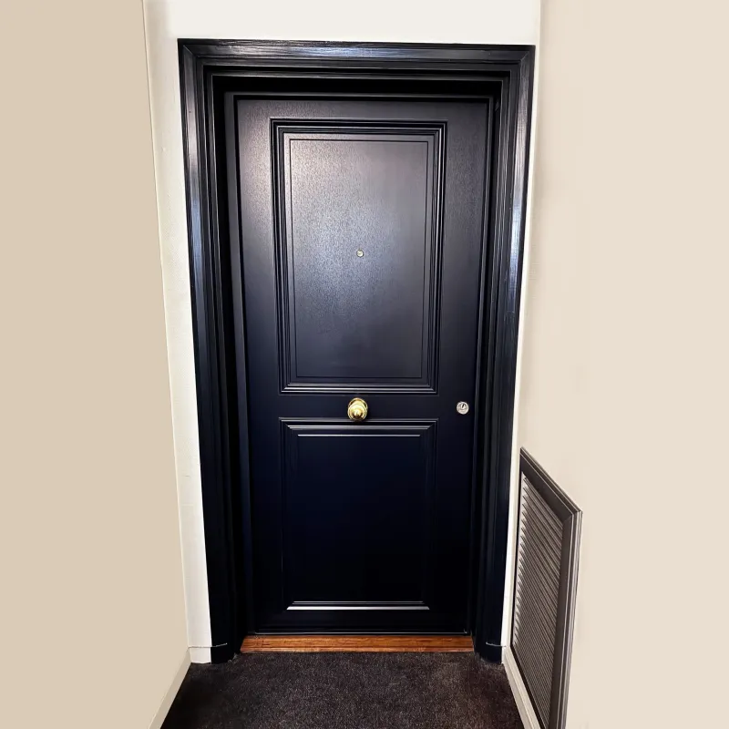 Porte blindée laquée noire à panneaux moulurés avec poignée et garnitures dorées, vue de face après installation